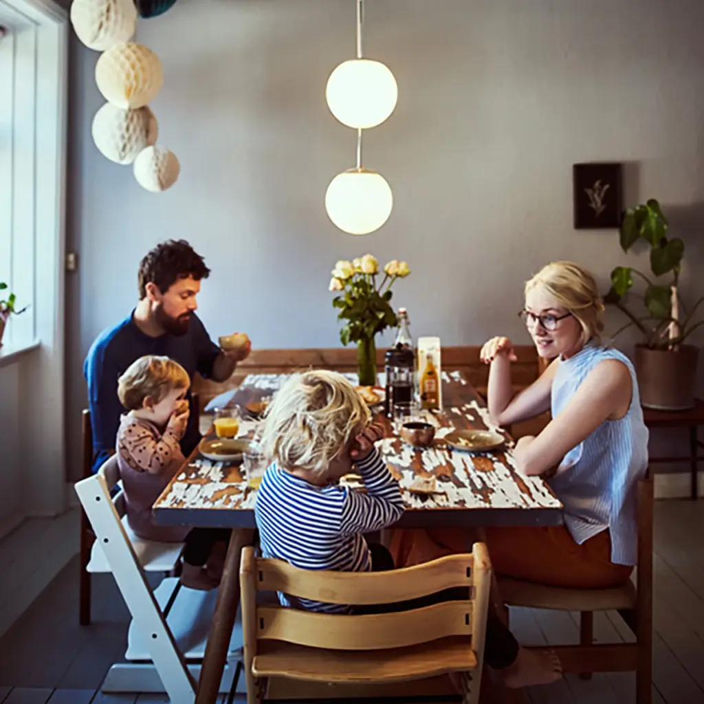 Familj som sitter runt ett matbord och äter tillsammans i ett kök