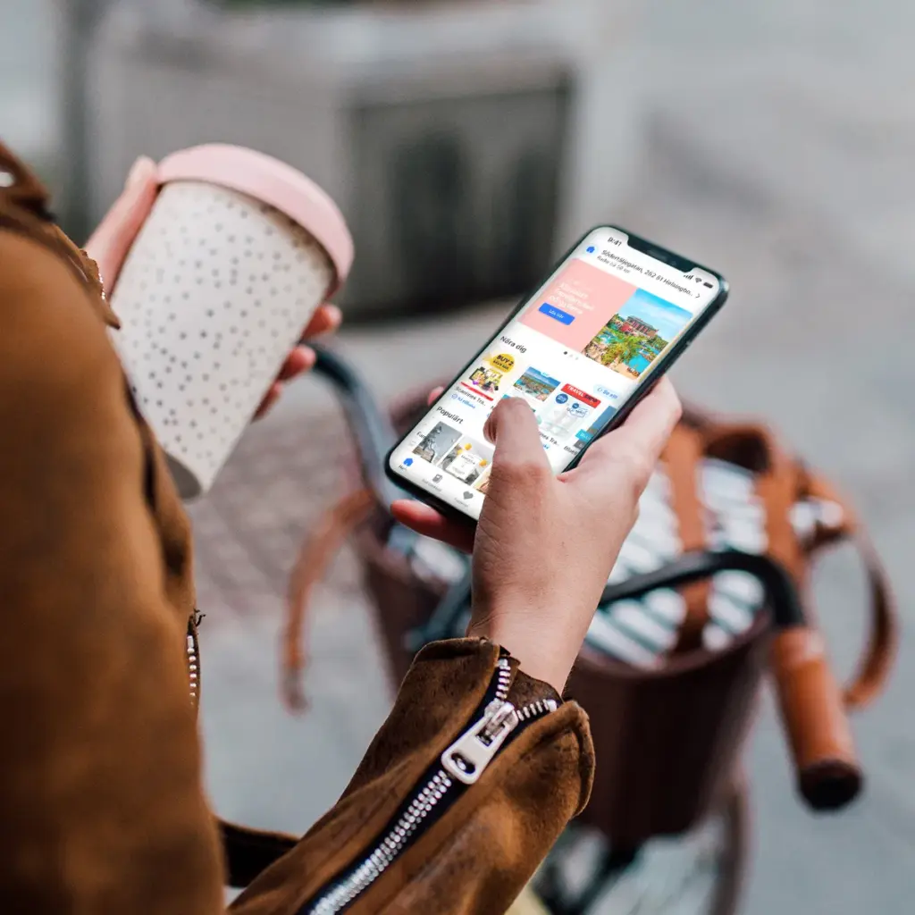 Person som håller en kaffemugg och använder Dayli-appen på en smartphone medan personen står vid en cykel