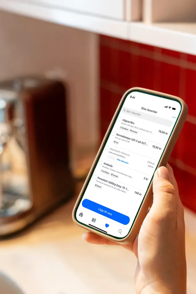 En person håller i en smartphone som visar en digital shoppinglista i en katalogapp i ett kök.